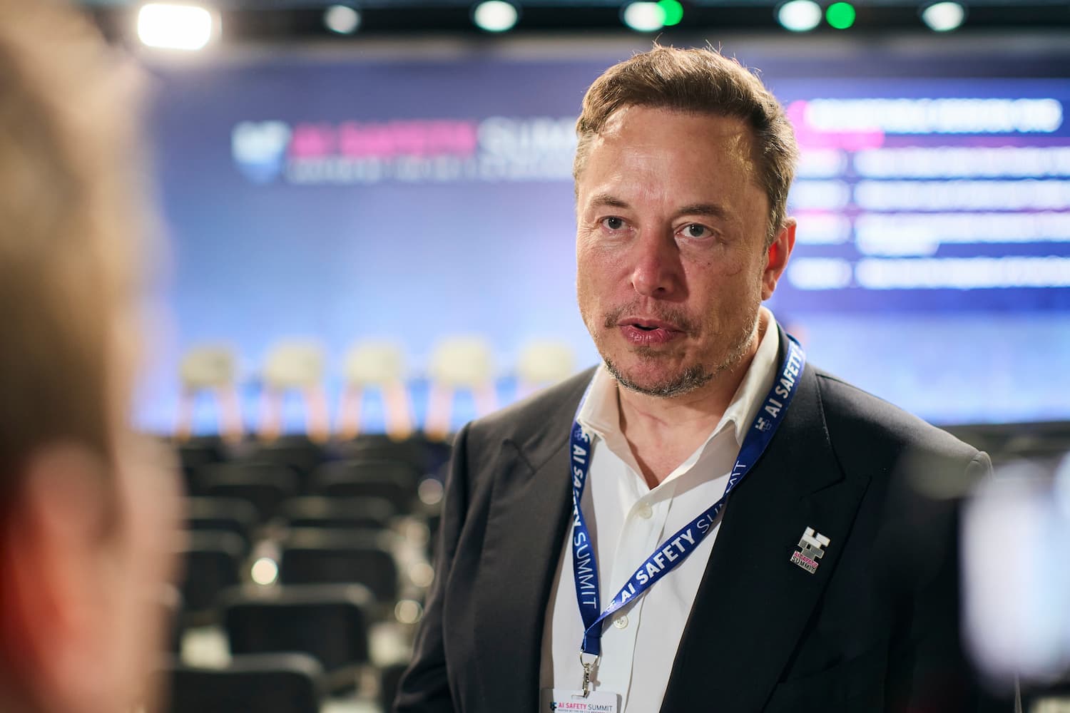 Elon Musk i en sal med en skjerm bak seg